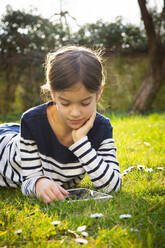 Portrait of little girl lying on a meadow using digital tablet - LVF08771