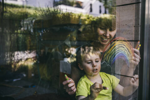 Mutter und kleiner Sohn zu Hause malen Regenbogen auf das Fenster, lizenzfreies Stockfoto