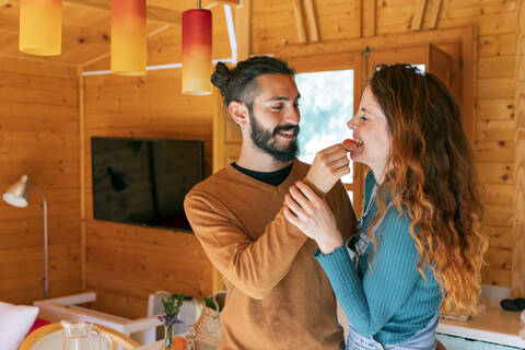 Glückliches junges Paar spielt mit einer Kirschtomate in einer Holzhütte, lizenzfreies Stockfoto