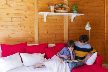 Mutter und Tochter lesen ein Buch auf einer Couch in einer Holzhütte - VSMF00034