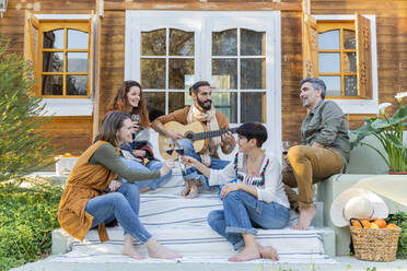 Friends playing music on the guitar and drinking wine outside a cabin in the countryside - VSMF00050