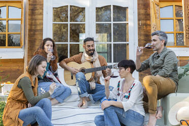 Freunde musizieren auf der Gitarre und trinken Wein vor einer Hütte auf dem Lande - VSMF00051