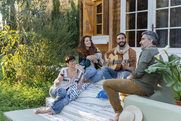 Friends playing music on the guitar and drinking wine outside a cabin in the countryside - VSMF00053
