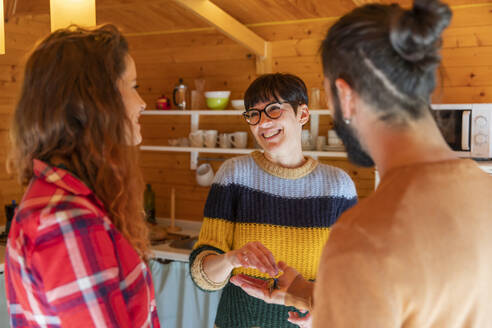 Host welcoming young couple in a cabin in the countryside handing over house key - VSMF00066