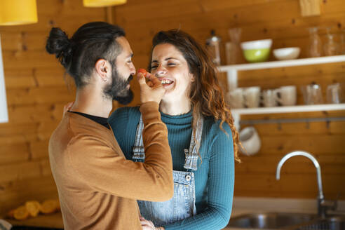 Glückliches junges Paar spielt mit einer Kirschtomate in einer Holzhütte - VSMF00087