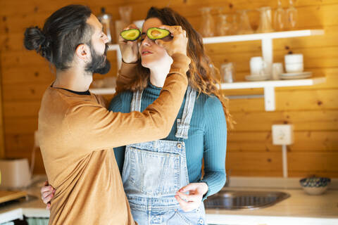Verspieltes junges Paar hat Spaß mit Avocados in einer Holzhütte, lizenzfreies Stockfoto
