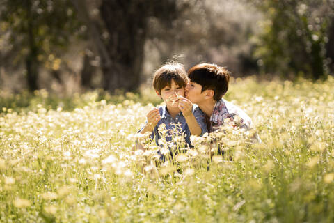 Mutter küsst Tochter in einem Feld mit Wildblumen, lizenzfreies Stockfoto