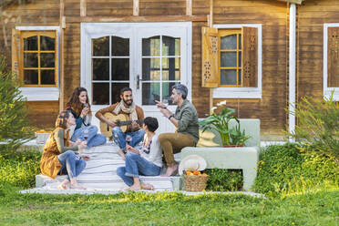 Friends playing music on the guitar and drinking wine outside a cabin in the countryside - VSMF00163