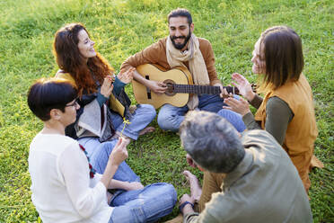 Gruppe von Freunden, die im Gras sitzend auf einem Feld mit der Gitarre Musik machen - VSMF00164