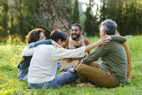 Eine Gruppe von Freunden spielt Musik und umarmt sich im Gras auf einem Feld, lizenzfreies Stockfoto