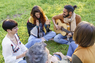 Gruppe von Freunden, die im Gras sitzend auf einem Feld mit der Gitarre Musik machen - VSMF00166