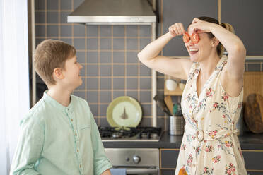 Junge beobachtet seine Mutter, die sich in der Küche die Augen mit Tomatenscheiben bedeckt - VPIF02214