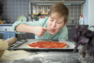 Porträt eines Jungen, der in der Küche Tomatensoße knabbert - VPIF02217