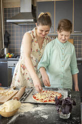 Mutter und Sohn streuen geriebenen Käse auf den Pizzaboden - VPIF02220