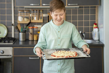 Porträt eines stolzen Jungen, der ein Backblech mit roher hausgemachter Pizza hält - VPIF02221