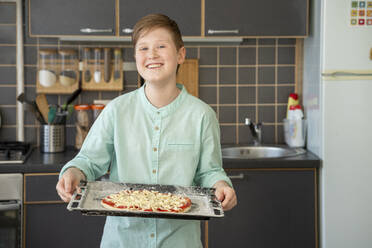 Porträt eines stolzen Jungen, der ein Backblech mit roher hausgemachter Pizza hält - VPIF02222