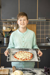 Porträt eines lächelnden Jungen, der ein Backblech mit roher hausgemachter Pizza hält - VPIF02223