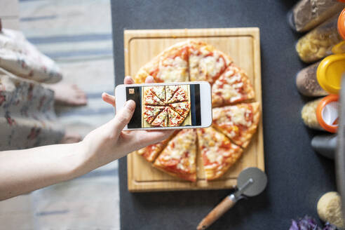 Ausschnittansicht einer Frau, die mit ihrem Smartphone eine selbstgemachte Pizza fotografiert - VPIF02230