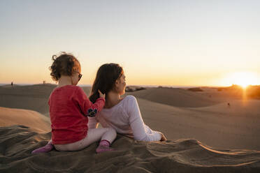 Mother and daughter relaxing in sand dunes at sunset, Gran Canaria, Spain - DIGF09553