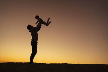 Father playing with daughter on sand dune at sunset, Gran Canaria, Spain - DIGF09556