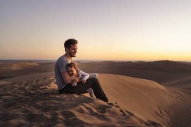 Happy father sitting with daughter in sand dunes at sunset, Gran Canaria, Spain - DIGF09563