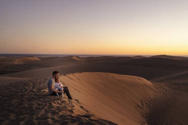 Vater sitzt mit Tochter in Sanddünen bei Sonnenuntergang, Gran Canaria, Spanien - DIGF09565