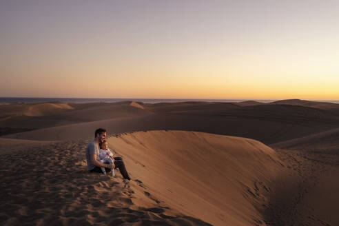 Father sitting with daughter in sand dunes at sunset, Gran Canaria, Spain - DIGF09565
