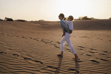 Mother carrying daughter piggyback in sand dunes, Gran Canaria, Spain - DIGF09581