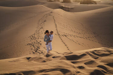 Mother carrying daughter in sand dunes, Gran Canaria, Spain - DIGF09588