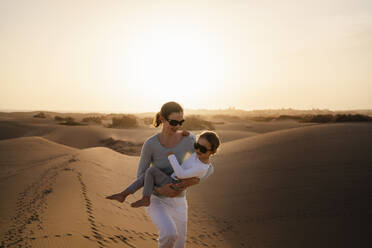 Mother carrying daughter in sand dunes at sunset, Gran Canaria, Spain - DIGF09589