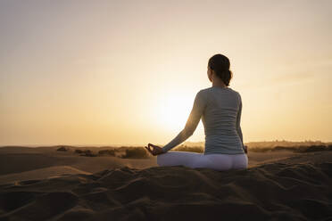 Woman practicing yoga in sand dunes at sunset, Gran Canaria, Spain - DIGF09603