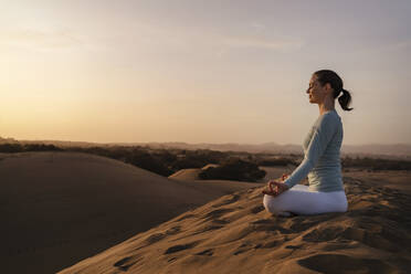 Woman practicing yoga in sand dunes at sunset, Gran Canaria, Spain - DIGF09606