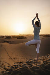 Woman practicing yoga in sand dunes at sunset, Gran Canaria, Spain - DIGF09611