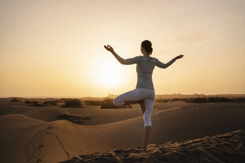 Woman practicing yoga in sand dunes at sunset, Gran Canaria, Spain - DIGF09612