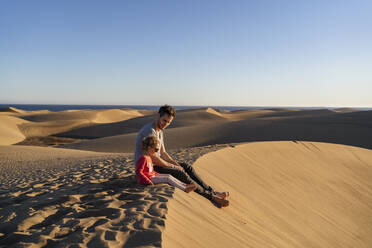 Father and daughter sitting on sand dune, Gran Canaria, Spain - DIGF09623