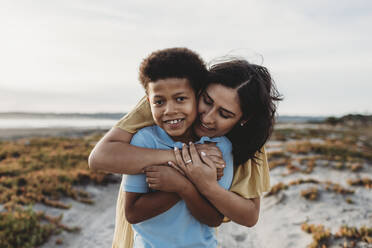 Front view close up portrait of young mother embracing son beach - CAVF78998