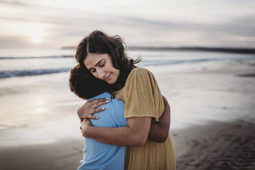 Side view of beautiful mother hugging son at seashore during sunset - CAVF79001