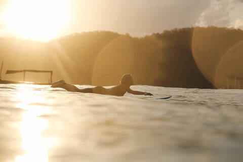 Weibliche Surferin im Meer bei Sonnenuntergang, lizenzfreies Stockfoto