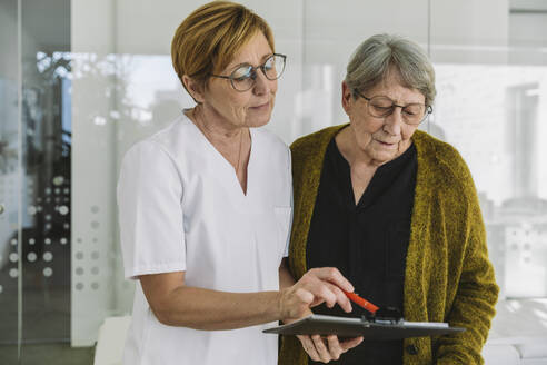 Medizinische Sekretärin hilft älteren Patienten beim Ausfüllen eines Dokuments - MFF05428