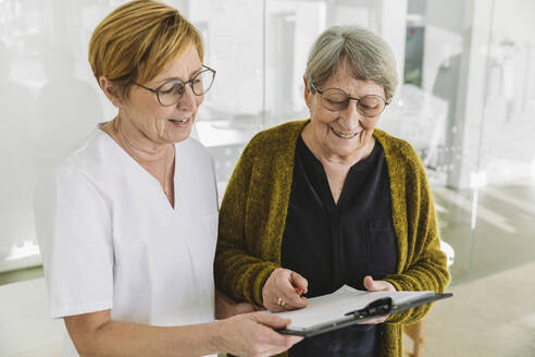 Medizinische Sekretärin hilft älteren Patienten beim Ausfüllen eines Dokuments - MFF05430
