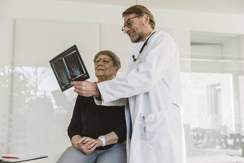 Arzt bespricht das Röntgenbild einer gebrochenen Hand mit einem älteren Patienten - MFF05434