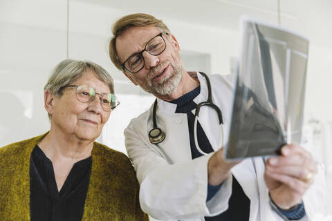 Arzt bespricht Röntgenbild mit älterem Patienten, lizenzfreies Stockfoto