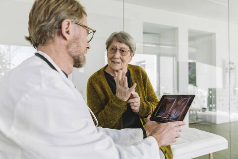 Arzt bespricht das Röntgenbild einer gebrochenen Hand mit einem älteren Patienten, lizenzfreies Stockfoto