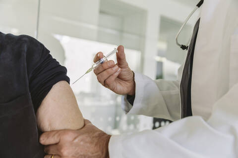 Arzt injiziert Impfstoff in den Arm eines älteren Patienten, lizenzfreies Stockfoto