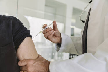 Doctor injecting vaccine into senior patient’s arm - MFF05451