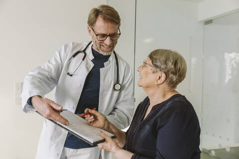 Arzt hilft älterem Patienten beim Ausfüllen eines Dokuments, lizenzfreies Stockfoto