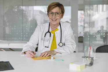 Porträt eines lächelnden Arztes, der einen Impfpass ausfüllt - MFF05487