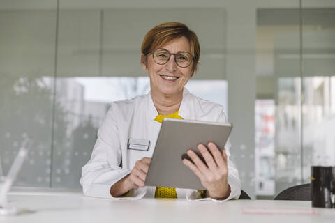 Portrait of smiling doctor sitting at desk using tablet stock photo