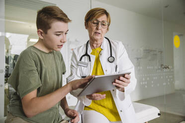 Doctor showing tablet to teenage boy in medical practice - MFF05513