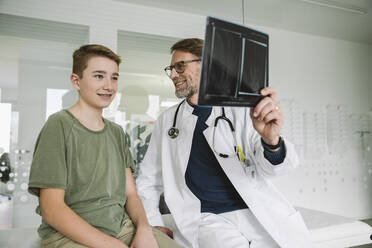 Doctor explaining x-ray image of broken hand to teenage boy in medical practice - MFF05515